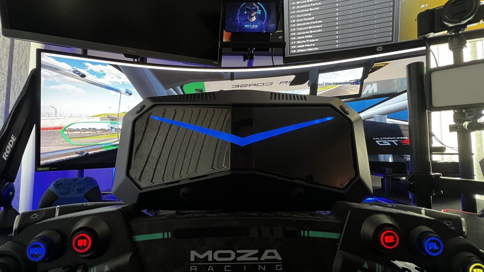 View from inside a triple-monitor sim racing cockpit with a Moza Racing wheel and Pimax headset mount